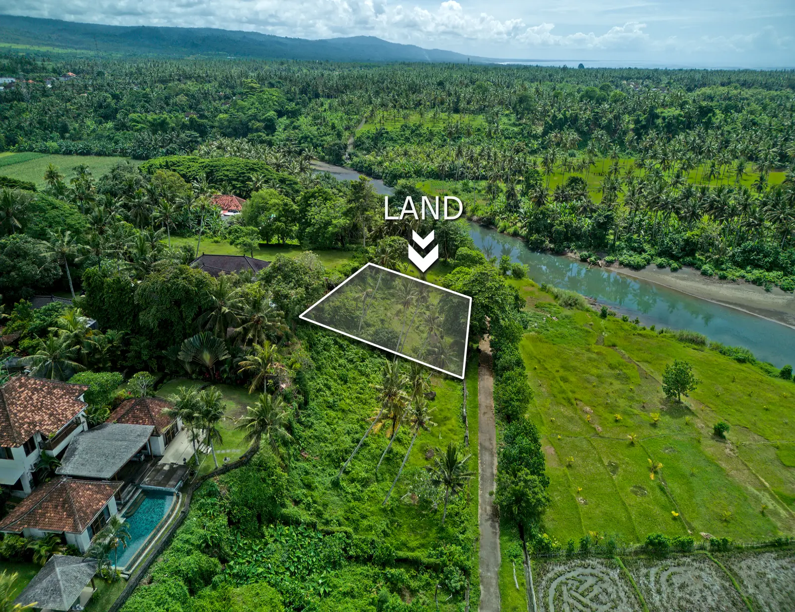 Drone shot of Pulukan riverside land overlooking tropical forest and nearby rice fields.