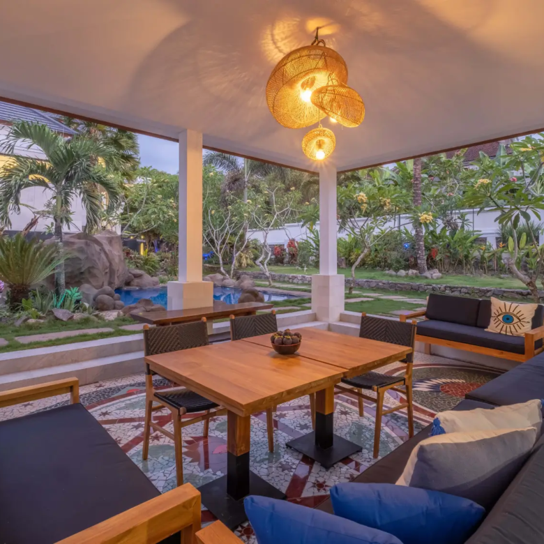 Open-air dining pavilion in Bali villa overlooking tropical garden and rock-feature pool.