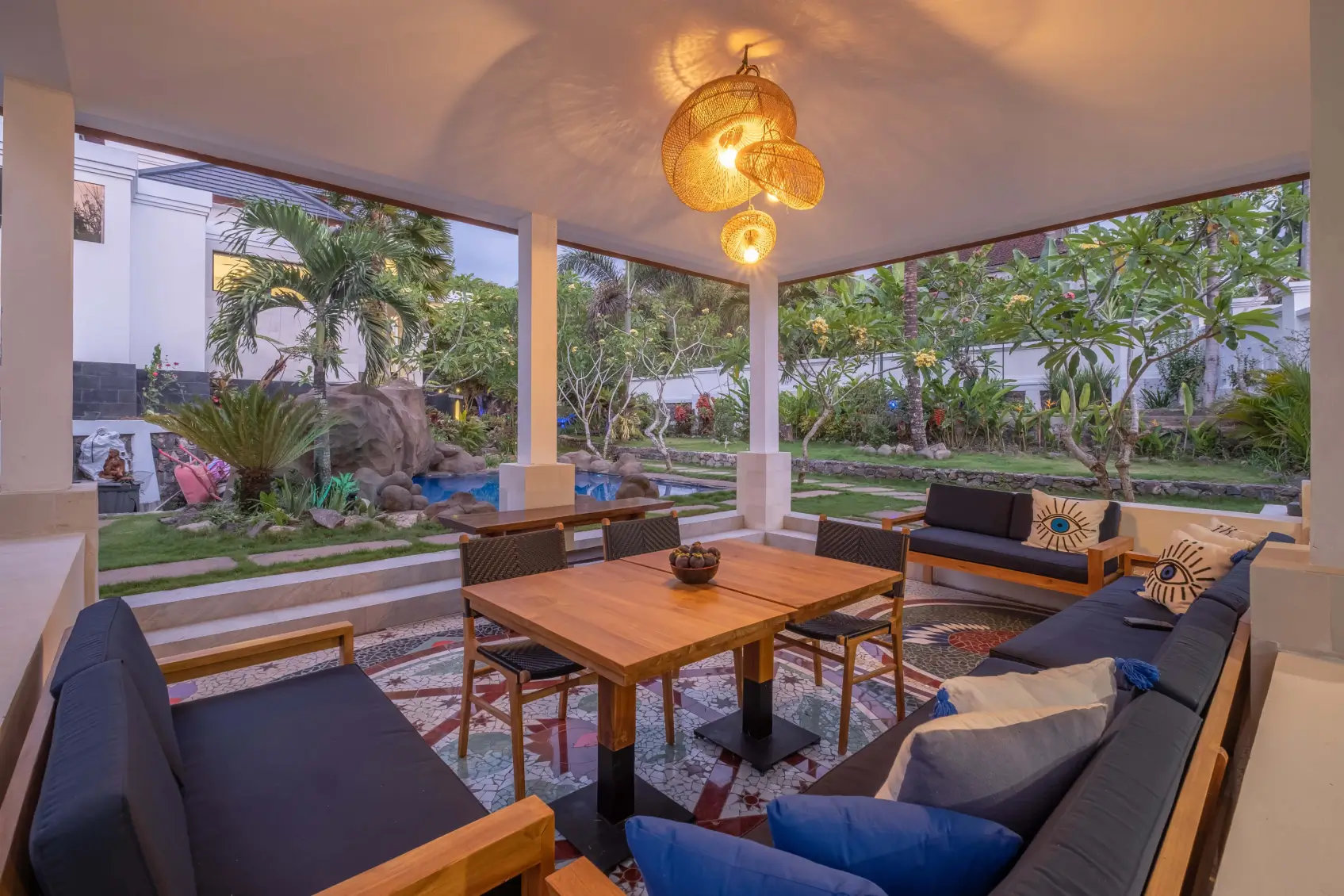 Open-air dining pavilion in Bali villa overlooking tropical garden and rock-feature pool.