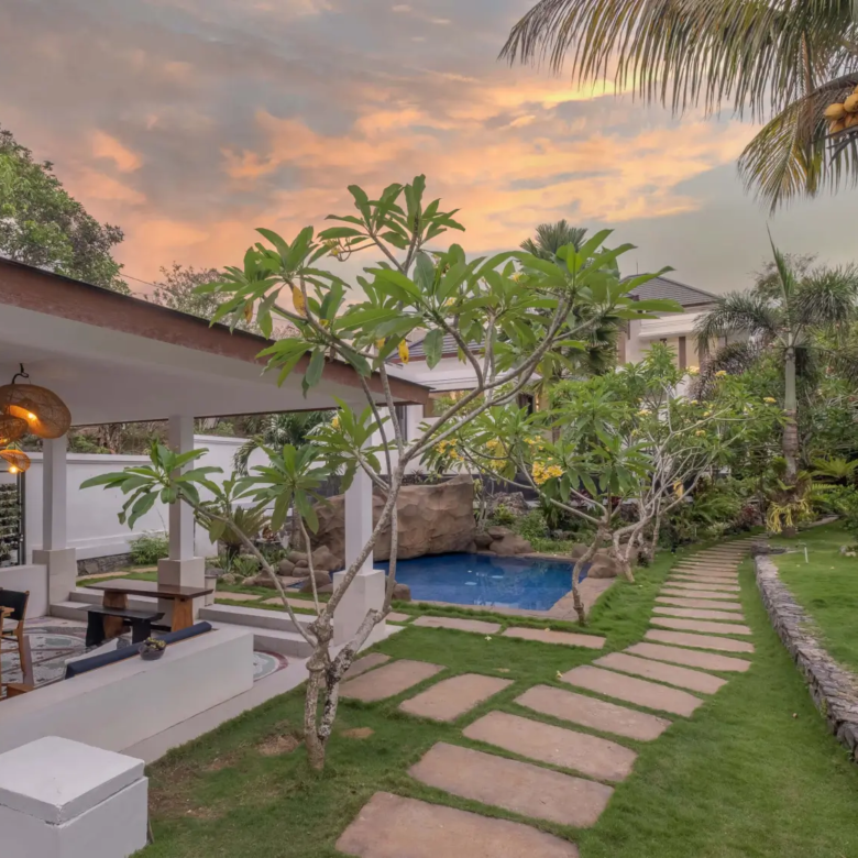 Tropical Bali villa garden with stone walkway, coconut trees, and private rock-feature swimming pool.