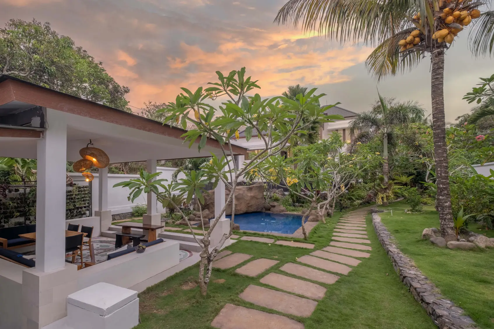 Tropical Bali villa garden with stone walkway, coconut trees, and private rock-feature swimming pool.