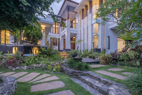 Modern luxury villa in Bali with landscaped tropical garden and stone pathway at sunset.