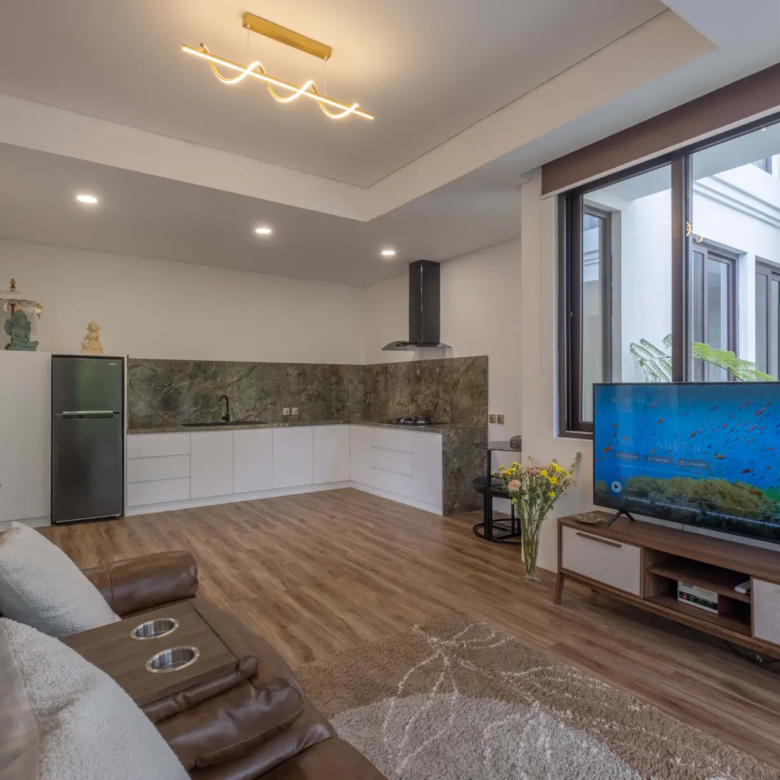 Spacious modern living room and kitchen in Bali villa with wood flooring and large windows.