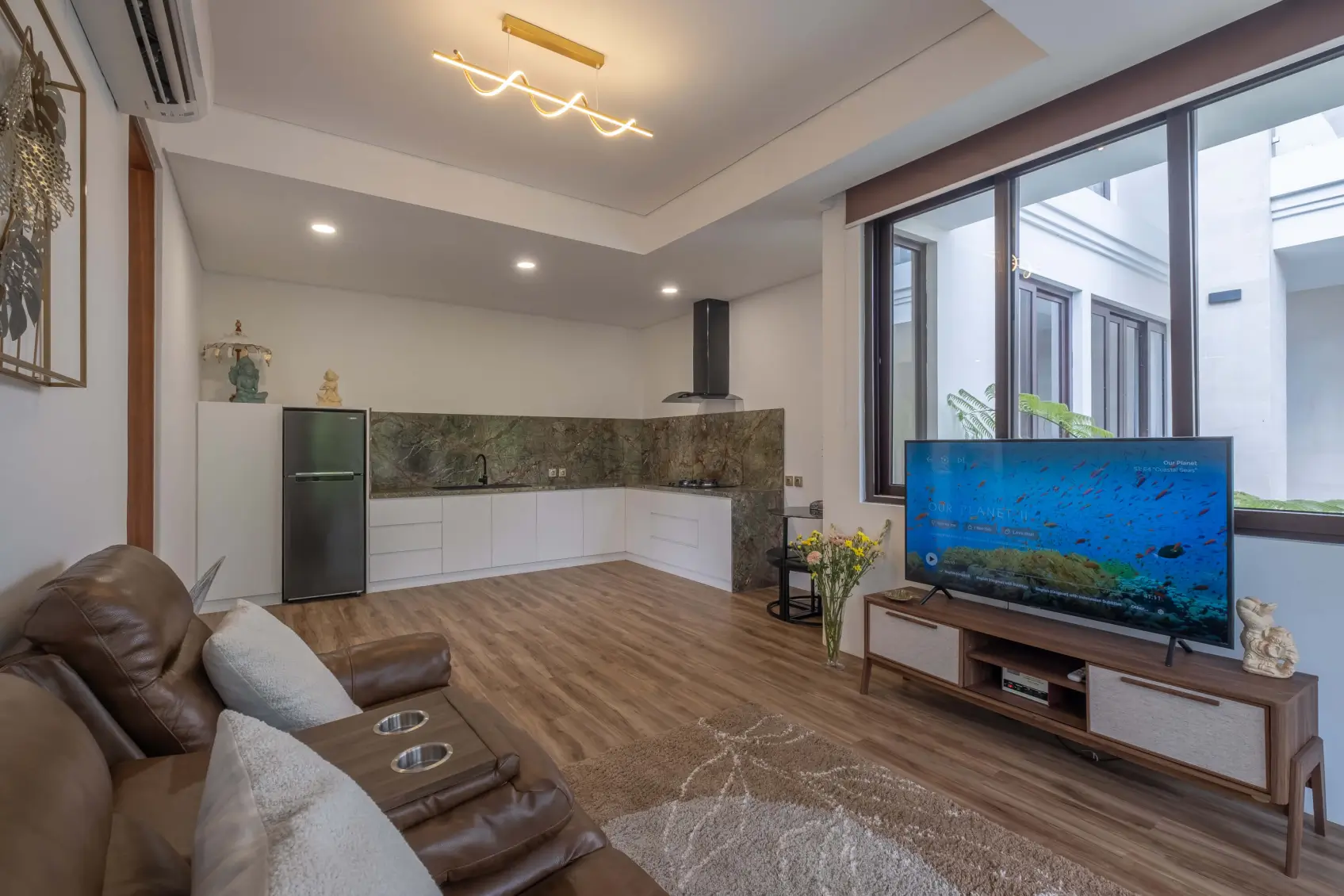 Spacious modern living room and kitchen in Bali villa with wood flooring and large windows.