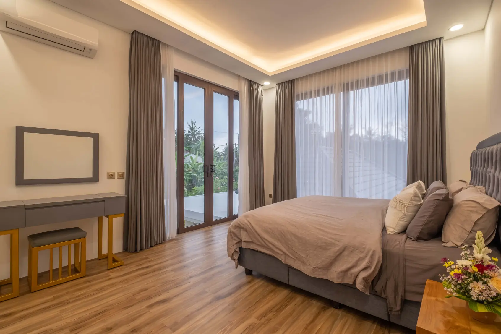 Contemporary Bali bedroom with large windows, balcony access, soft lighting, and garden views.