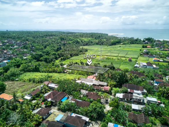 Aerial view of 1070m² land for sale in Pulukan, Bali, surrounded by green ricefields, village homes, and ocean views in the distance.