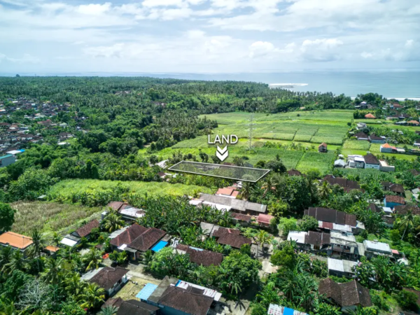 Aerial view of 1070m² land for sale in Pulukan, Bali, surrounded by green ricefields, village homes, and ocean views in the distance.