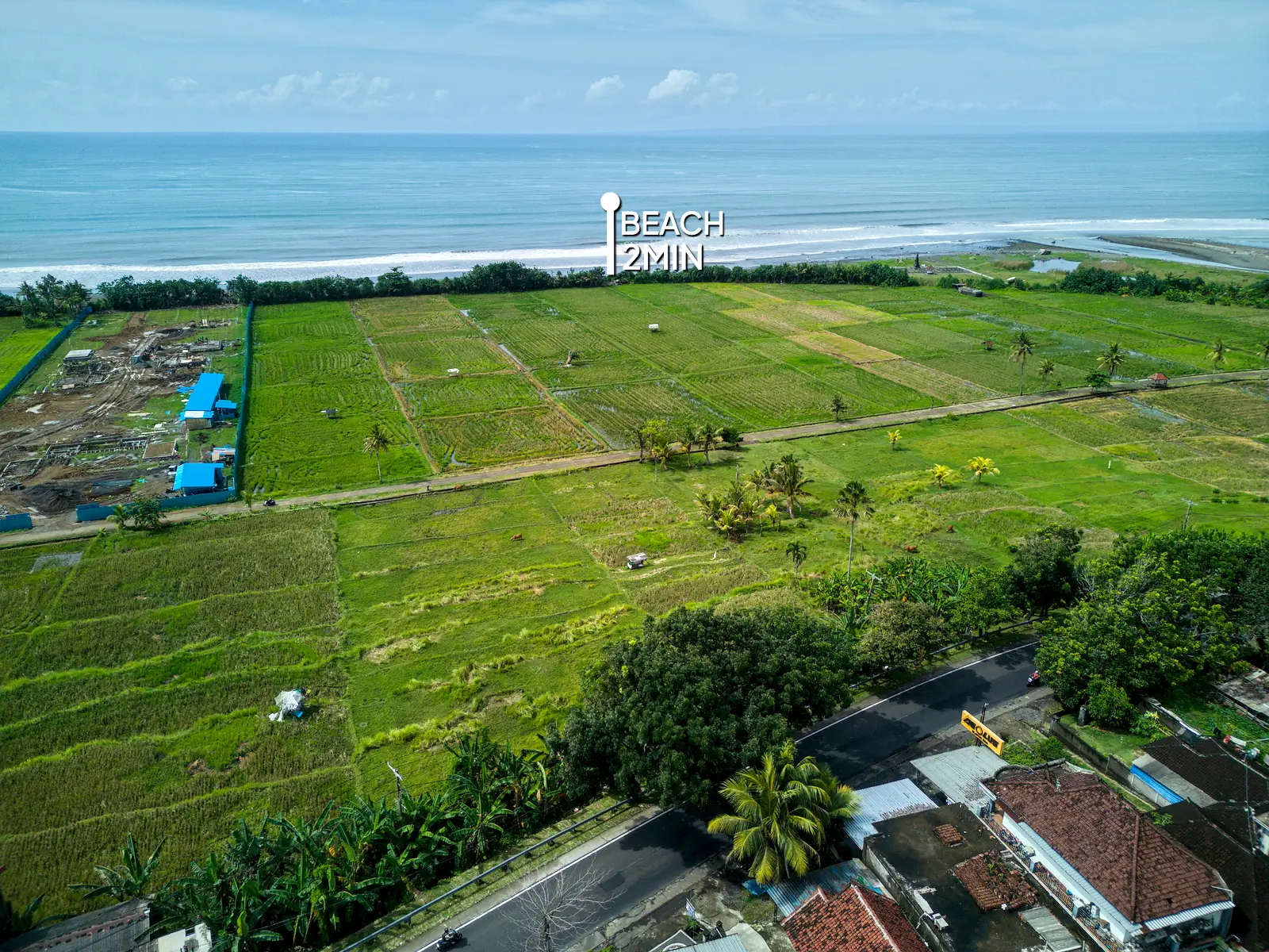 Panoramic aerial view of West Bali land for sale just 2 minutes from the beach, overlooking rice terraces and coastal landscape with nearby development area.