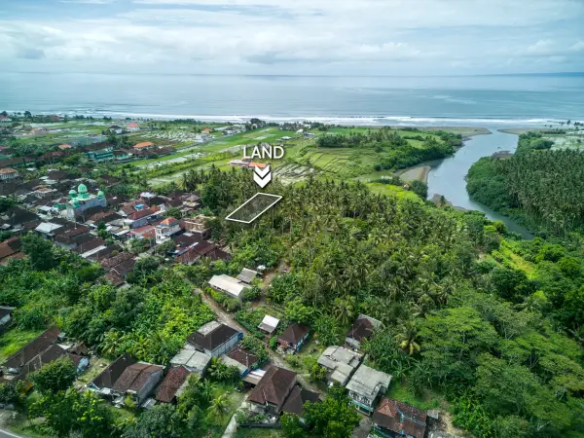 Aerial view of a 1350 m² land plot for sale in West Bali, located near the beach and surrounded by lush coconut trees and a traditional village