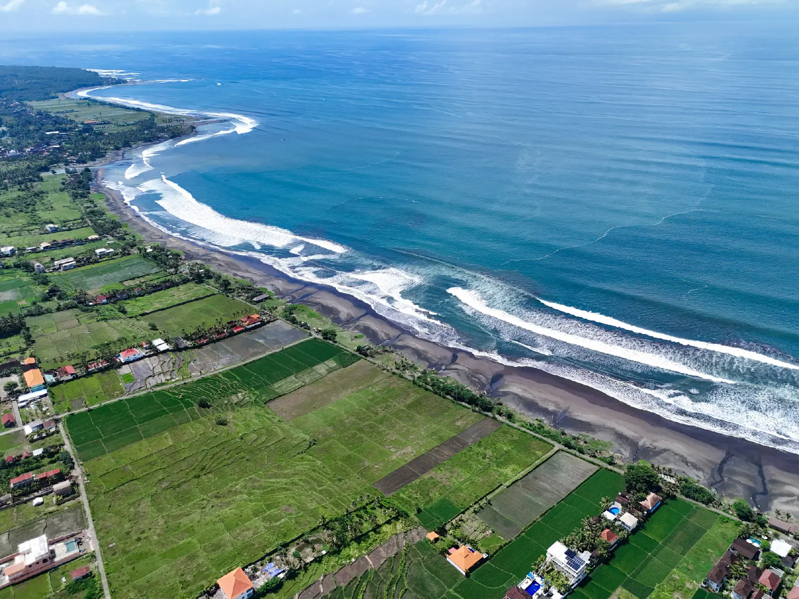 Panoramic aerial view of West Bali’s coastline featuring long black-sand beaches, ocean waves, and expansive green farming land