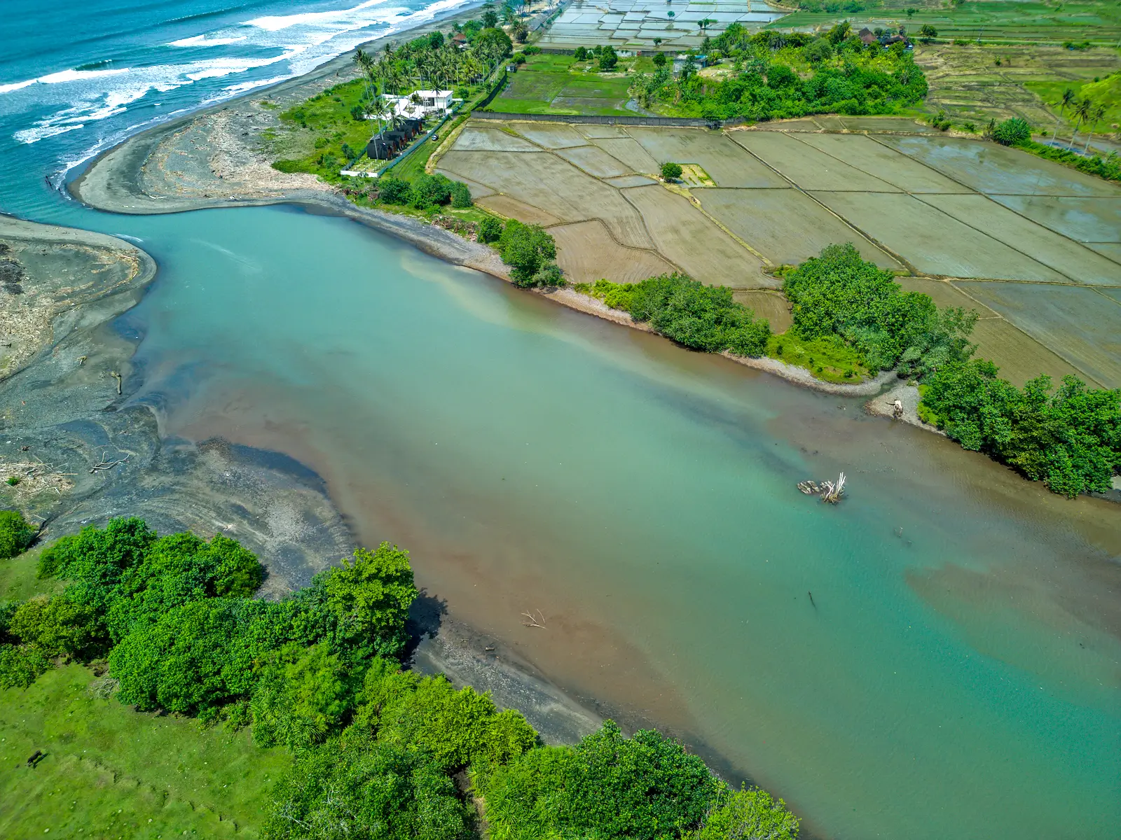 yehsumbul 5-5-00010 Scenic aerial view of the turquoise lagoon meeting the ocean in West Bali, highlighting natural coastal beauty, sandy shoreline, and nearby agricultural landscape.