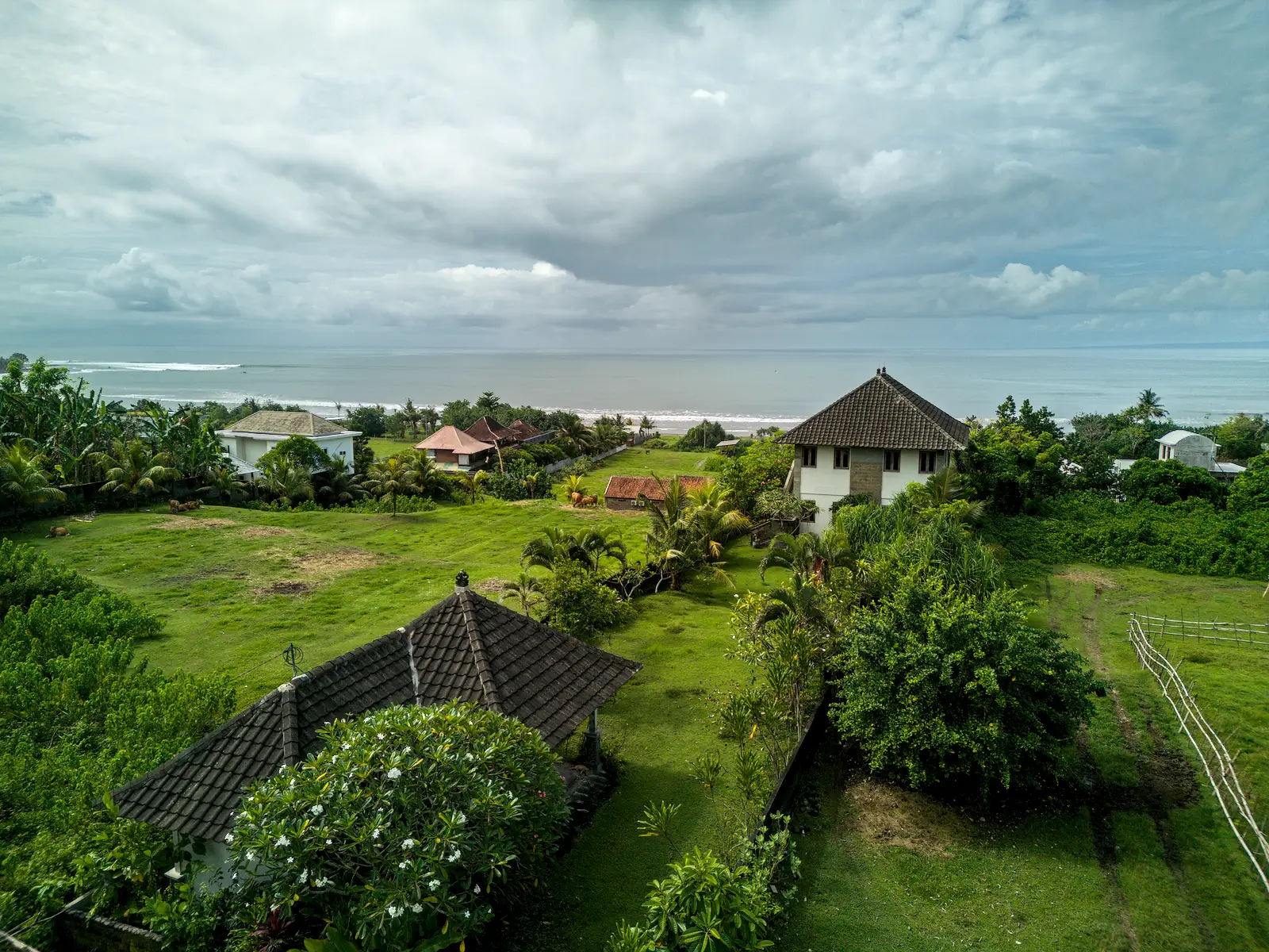 yehsumbul 6-00008 Ground-level view from a land plot in West Bali, featuring surrounding villas, tropical gardens, and ocean waves visible on the horizon