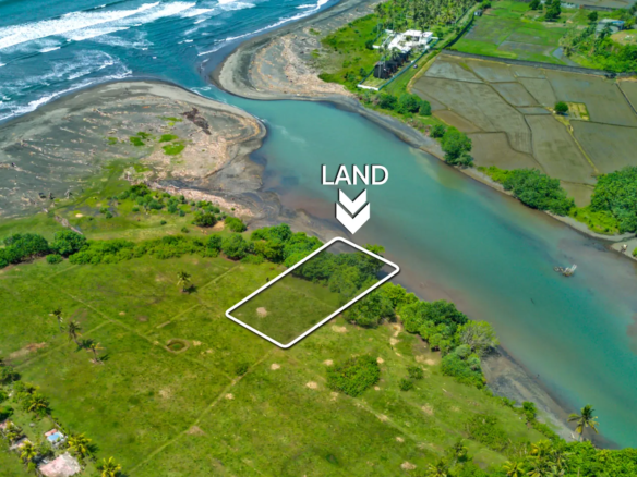 Aerial view of a 1,000 m² riverfront land plot in West Bali, located steps from the beach with turquoise lagoon water, ocean waves, and open green fields.