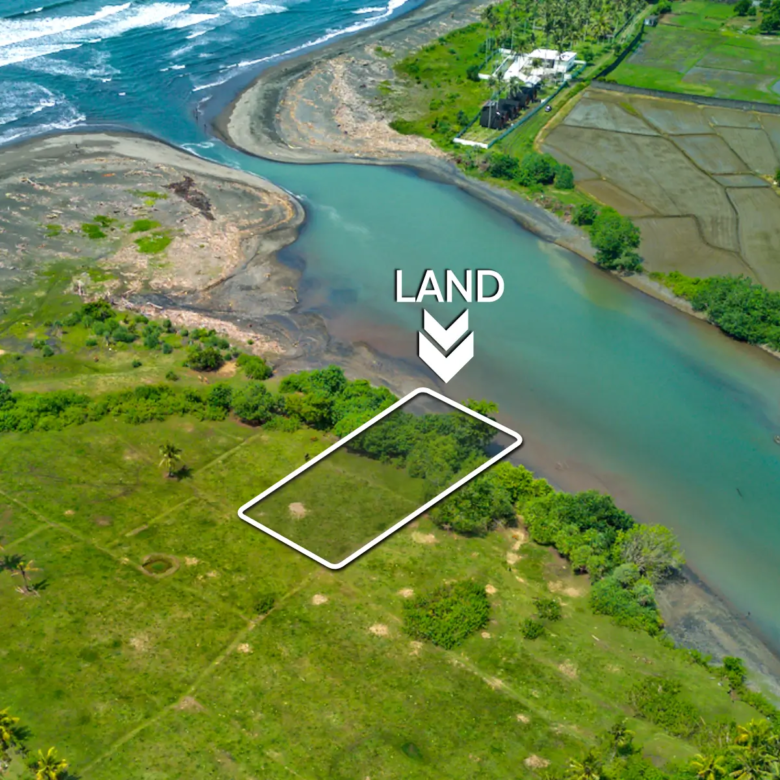 Aerial view of a 1,000 m² riverfront land plot in West Bali, located steps from the beach with turquoise lagoon water, ocean waves, and open green fields.