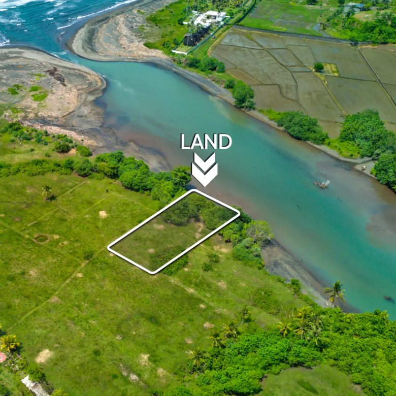 Aerial view of a 1,000 m² riverfront land plot in West Bali, located steps from the beach with turquoise lagoon water, ocean waves, and open green fields.