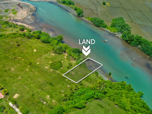 erial view of a 1,000 m² riverfront land plot in West Bali, located just steps from the beach with turquoise lagoon water, ocean waves, and surrounding green fields.